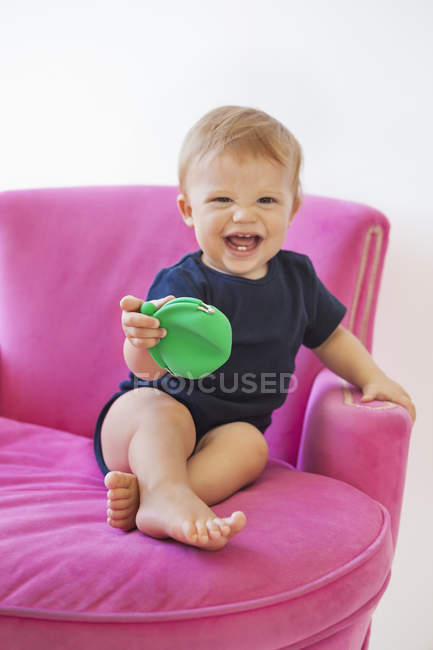 Дитячий хлопчик грає з сумкою, сидячи в рожевому кріслі — стокове фото