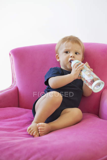 Малыш пьет воду из бутылки в розовом кресле — стоковое фото