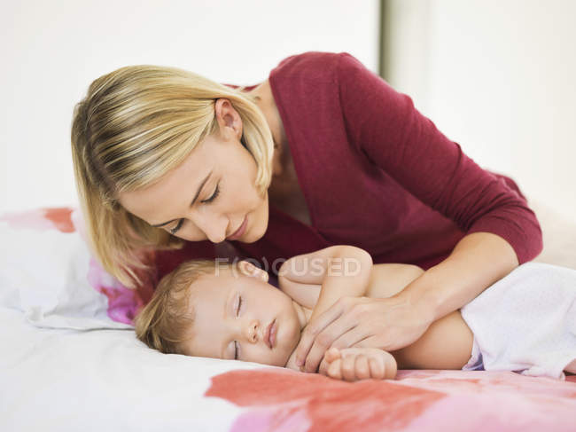 Pensativo jovem mulher olhando bonito bebê dormindo na cama — Fotografia de Stock