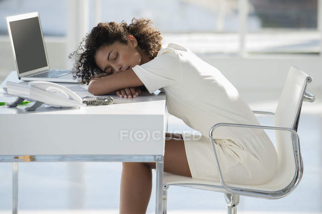 Mujer durmiendo con la cabeza descansando en el escritorio en la oficina - foto de stock