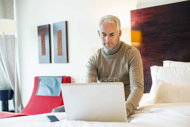 Homem maduro confiante usando laptop no quarto de hotel — Fotografia de Stock