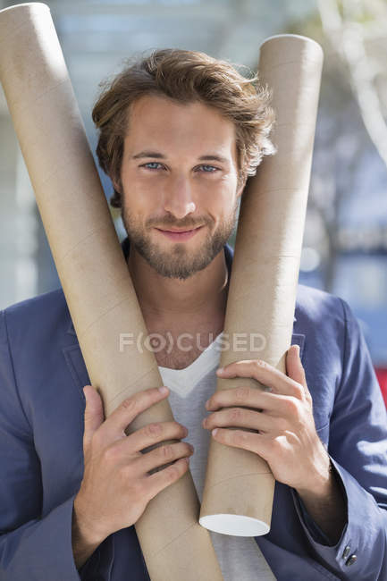 Portrait of male architect holding paper rolls and smiling — Stock Photo
