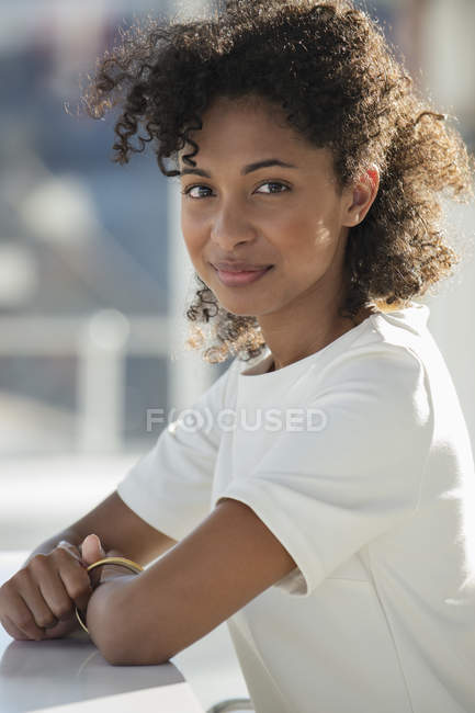 Retrato de mulher sorridente com penteado afro sorrindo sentado na mesa — Fotografia de Stock