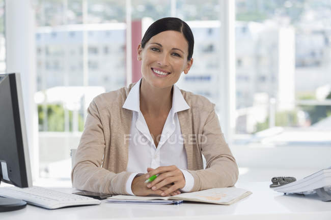 Retrato de empresaria confiada sonriendo en el escritorio en la oficina - foto de stock