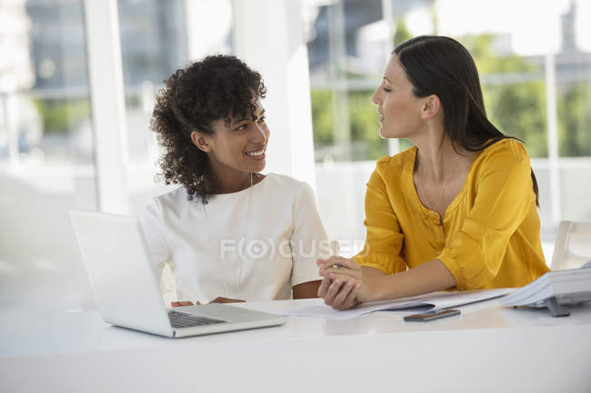 Дві усміхнені жінки сидять в офісі з ноутбуком — стокове фото