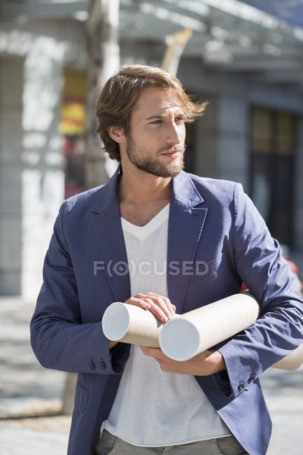 Architecte mâle portant des rouleaux de papier tout en marchant sur la rue — Photo de stock