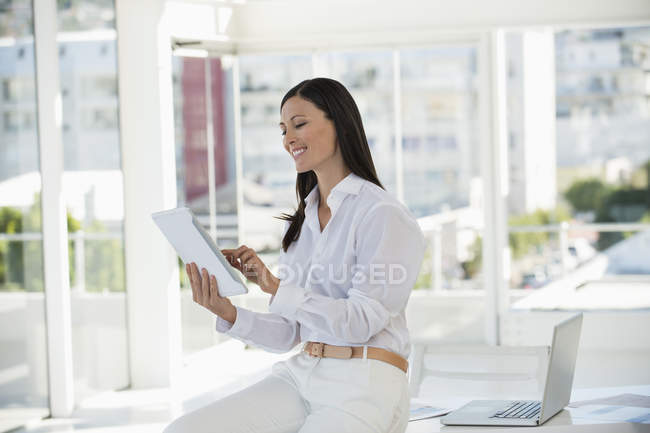 Empresária sorridente segurando tablet digital e sorrindo no escritório — Fotografia de Stock