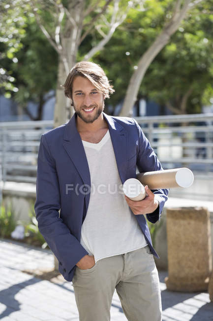 Portrait of architect carrying paper rolls and smiling on street — Stock Photo