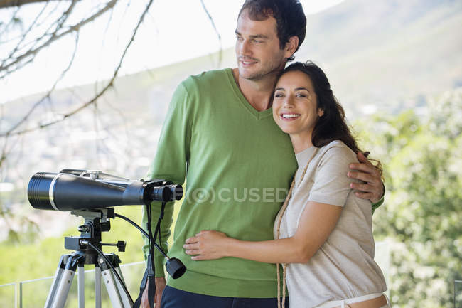 Пара улыбающихся рядом с биноклем на треноге в природе — стоковое фото