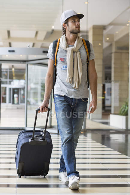 Young pensive man pulling luggage at airport — Stock Photo