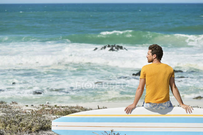 Чоловік сидить на дошці для серфінгу на пляжі і дивиться на камеру — стокове фото