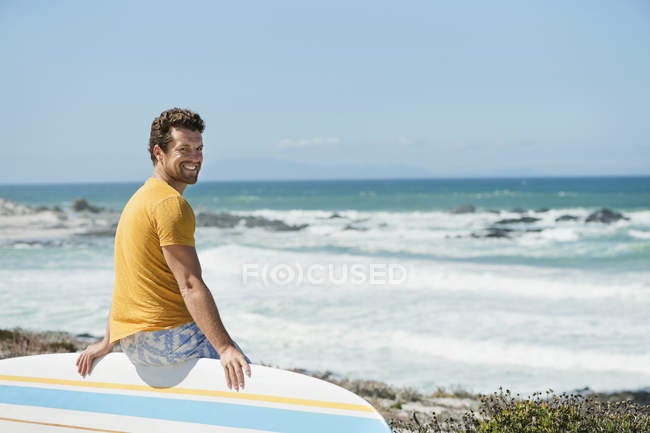 Чоловік сидить на дошці для серфінгу на пляжі і дивиться на камеру — стокове фото