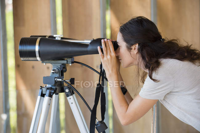 Woman looking through binoculars on tripod — Stock Photo