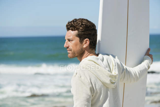 Человек держит доску для серфинга на волнистом море и смотрит в сторону — стоковое фото