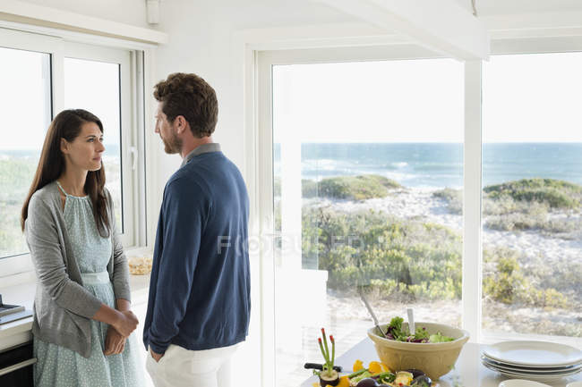 Casal conversando e olhando um para o outro na cozinha da casa costeira — Fotografia de Stock