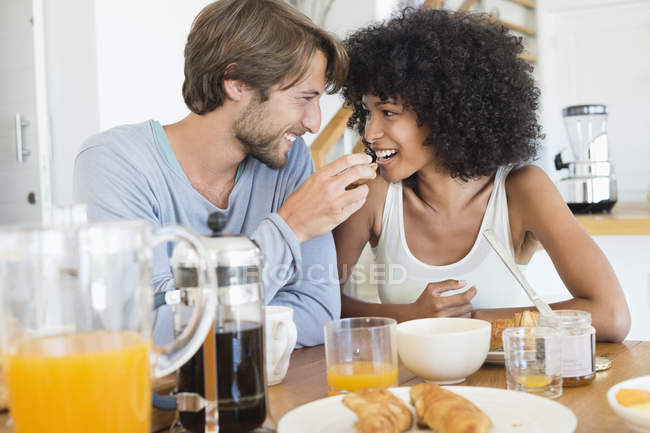 Мужчина кормит улыбающуюся жену на кухне — стоковое фото