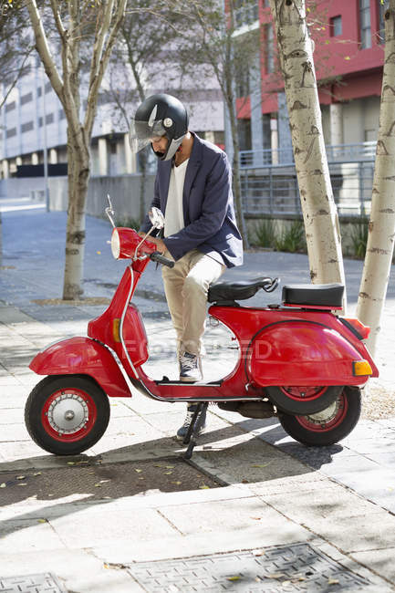 Человек в шлеме стоит с красным скутером на улице — стоковое фото