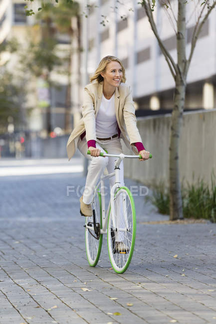 Sorrindo mulher loira andando de bicicleta em uma rua e sorrindo — Fotografia de Stock