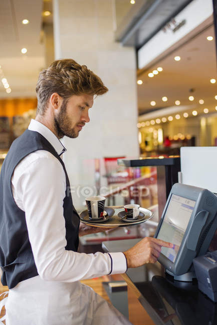 Camarero usando el ordenador en el mostrador de pago en un restaurante - foto de stock