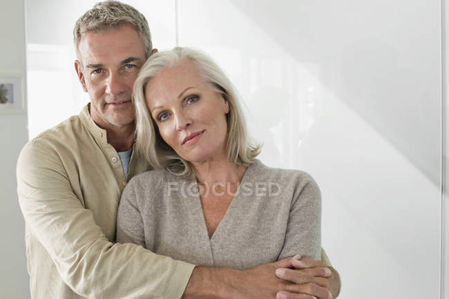 Retrato del hombre reflexivo abrazando esposa contra la pared blanca - foto de stock