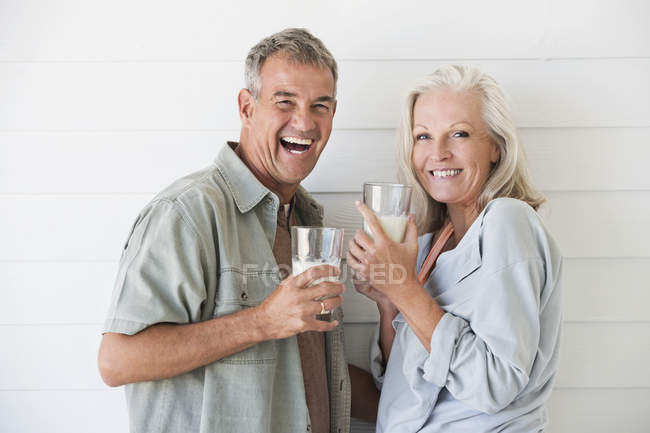 Portrait of laughing senior couple standing with glasses of milk — Stock Photo