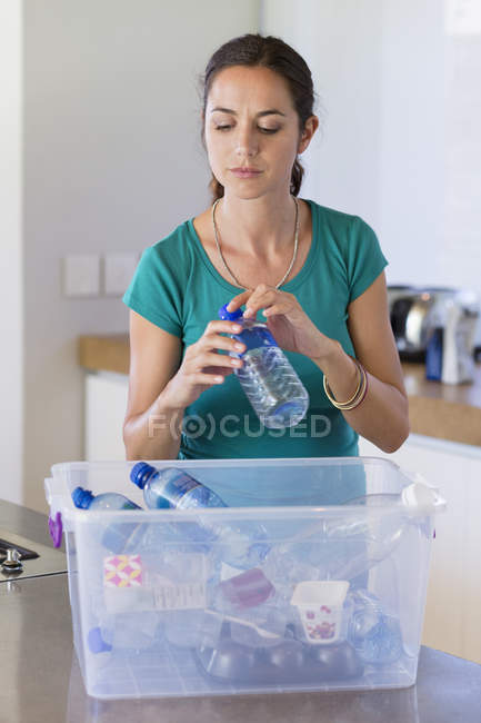 Woman putting bottle in recycling bin in kitchen — Stock Photo