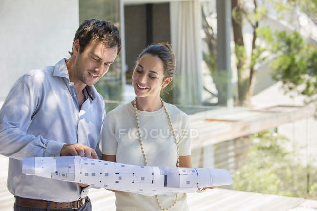 Couple looking at blueprint and smiling outdoors — Stock Photo