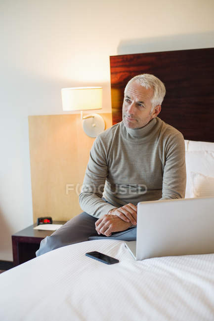 Man sitting with laptop on bed in a hotel room — Stock Photo
