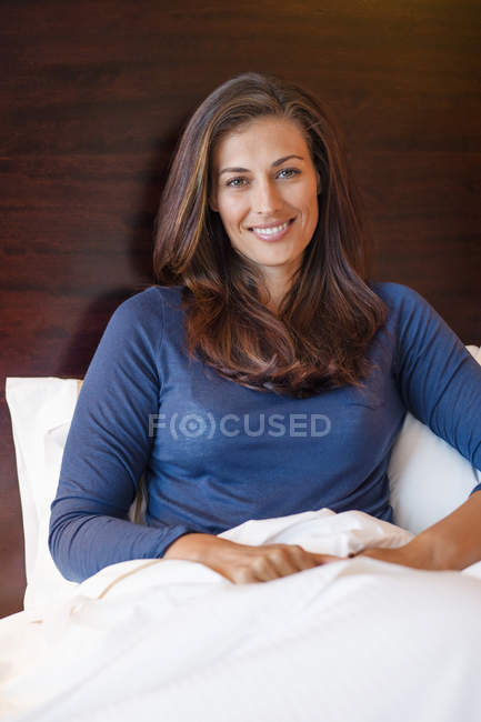 Retrato de una mujer sonriente sentada en la cama en la habitación del hotel - foto de stock