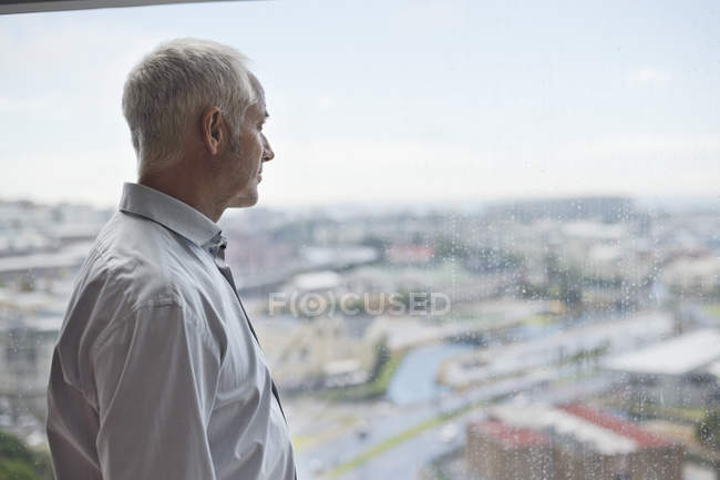 Задумливий старший чоловік дивиться через вікно — стокове фото