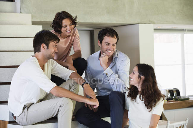 Smiling friends sitting on steps and talking — Stock Photo