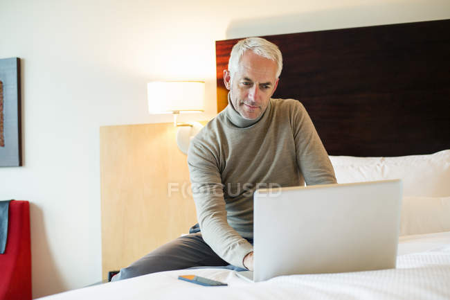 Uomo che utilizza un computer portatile sul letto in una camera d'albergo — Foto stock