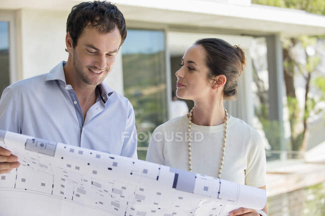 Couple looking at blueprint and smiling outdoors — Stock Photo
