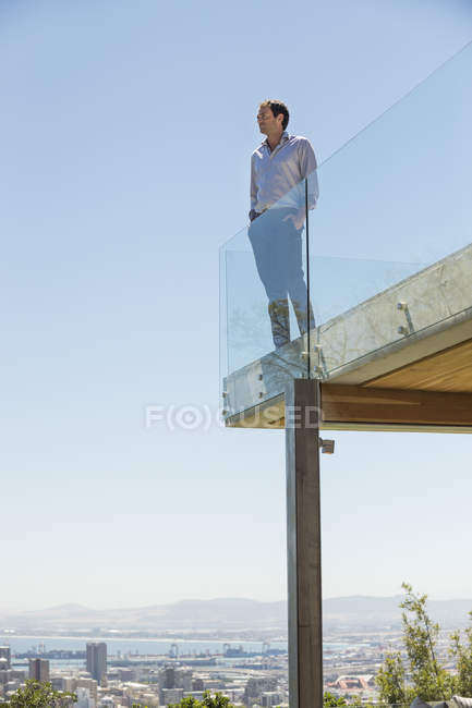 Чоловік стоїть на терасі зі скляним парканом з руками в кишенях — стокове фото