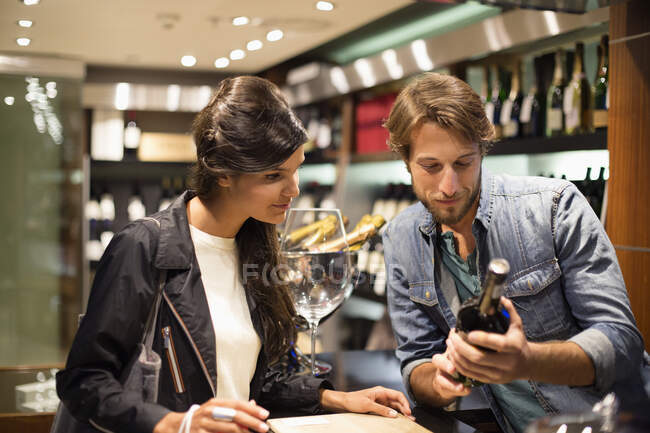 Commis aux ventes montrant une bouteille de vin à un client — Photo de stock