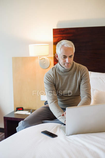 Homme utilisant un ordinateur portable sur le lit dans une chambre d'hôtel — Photo de stock