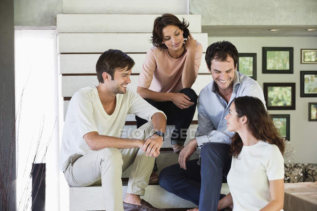 Lächelnde Freunde, die auf Stufen sitzen und reden — Stockfoto