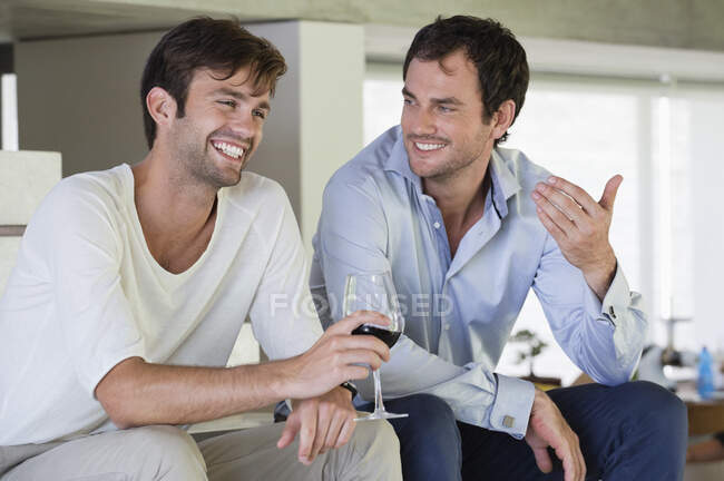 Sonrientes amigos varones con vino tinto - foto de stock