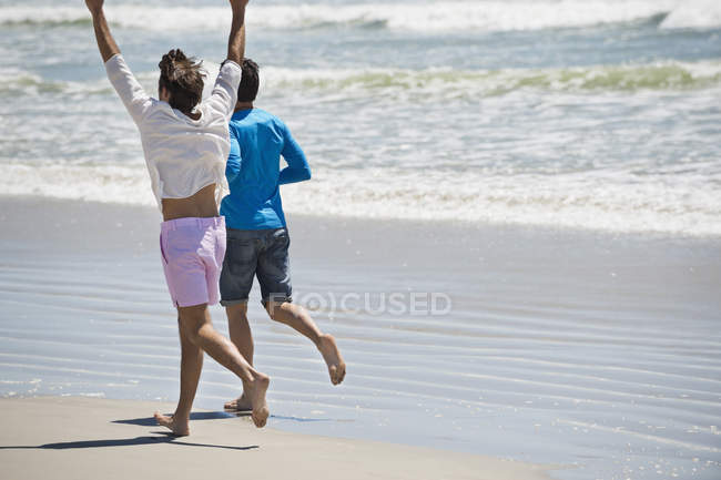 Homens felizes correndo na praia arenosa — Fotografia de Stock