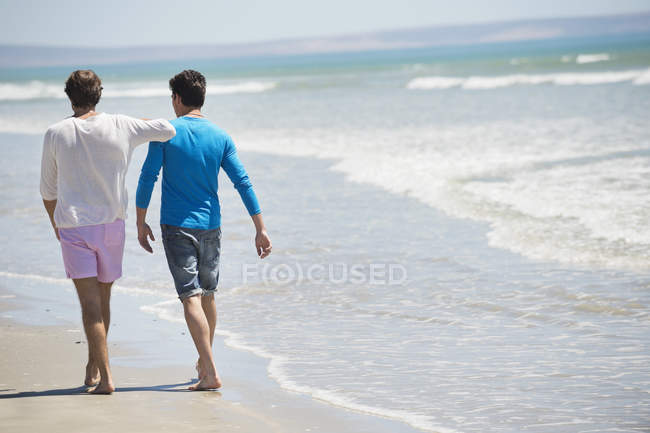 Hommes détendus marchant sur la plage avec mer ondulée — Photo de stock