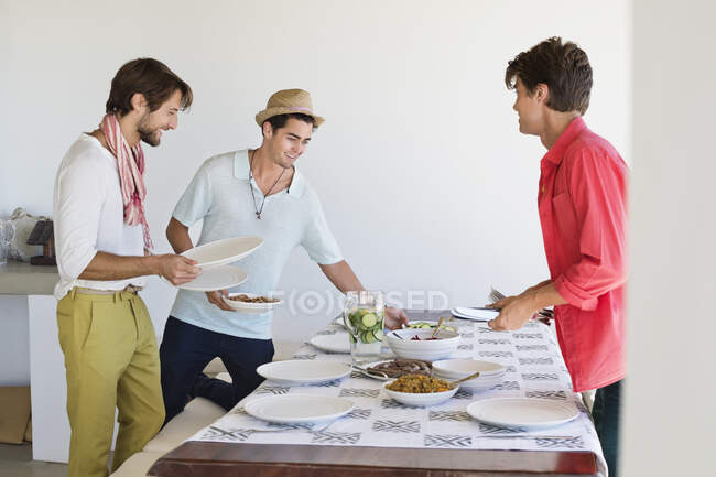 Amigos organizando comida en una mesa de comedor - foto de stock