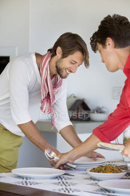 Friends arranging plates on a dining table — Stock Photo