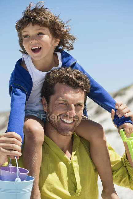 Человек, несущий своего сына на плечах на пляже — стоковое фото