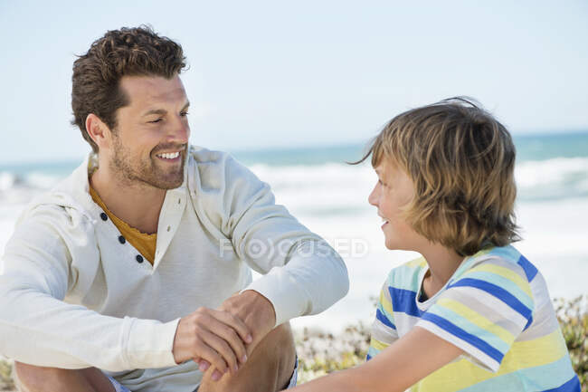 Человек, сидящий со своим сыном на пляже — стоковое фото