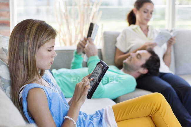 Fille utilisant une tablette numérique avec ses parents lisant des livres à la maison — Photo de stock