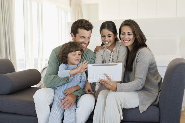Familia con niños compartiendo tableta digital en el sofá en casa - foto de stock