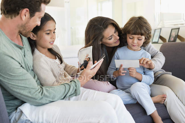 Padres mostrando fotografías a los niños en la sala de estar - foto de stock