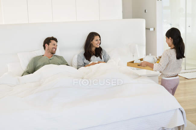 Girl serving tea to her parents on the bed — Stock Photo