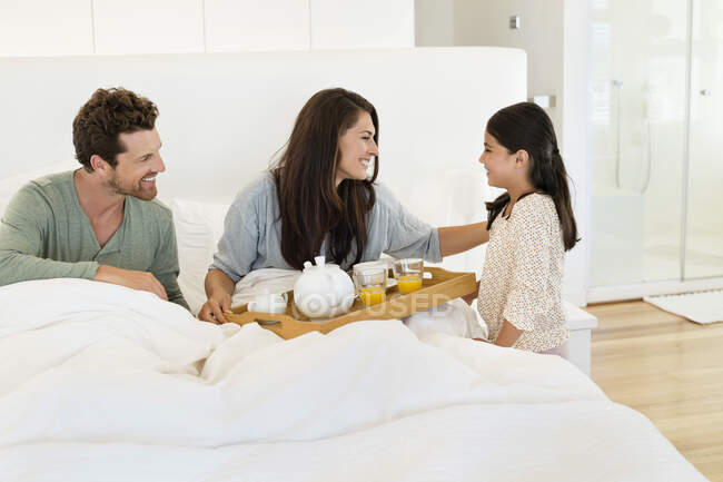 Mädchen serviert ihren Eltern Tee auf dem Bett — Stockfoto