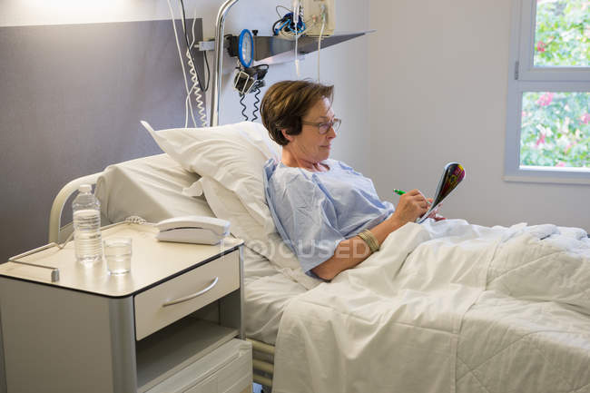 Woman writing in magazine on hospital bed — Stock Photo